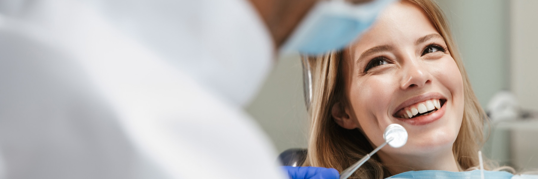 woman in dental chair during in-office dental treatment with dentist holding mirror tool nearby